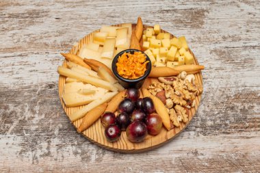 İçinde meyve, fındık ve çeşitli peynir içeren yuvarlak ahşap tepsi.