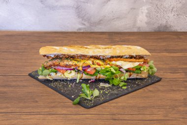 Eritilmiş peynirli harika bir pastırmalı sandviç, domates dilimleri, kuzu marulu ve lahanalı koyu kahverengi ahşap masa..