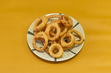 Kızarmış soğan halkalarıyla dolu bir porselen tabağı.