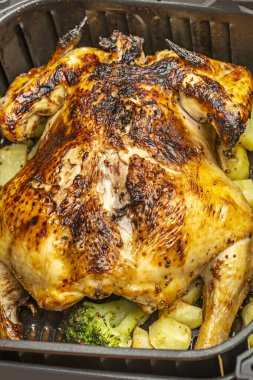 Kızarmış büyük bir tavuk, çıtır çıtır bir deriyle birlikte patates ve sebzelerle birlikte yeni pişmiş bir kızartma makinesinin içinde.