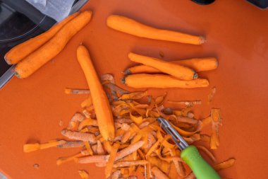 Turuncu mutfak tezgahında yeşil mango soyacağıyla havuç kesip soymak.