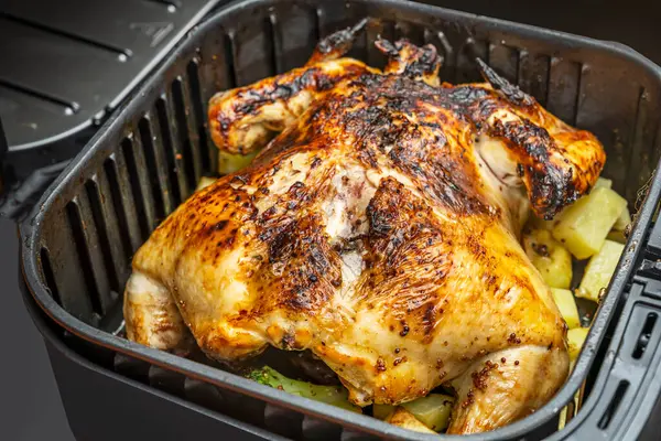 Kızarmış büyük bir tavuk, patates ve sebzelerle birlikte bir kızartma makinesinin içinde.