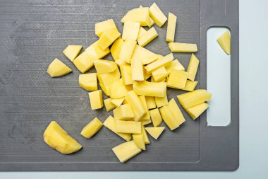Gri plastik bir kesme tahtasının üzerinde soyulmuş ve doğranmış patatesler.