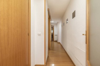 Dolu kıyafetleri olan bir koridor ve meşe döşemeli diğer odalara açılan kapılar.