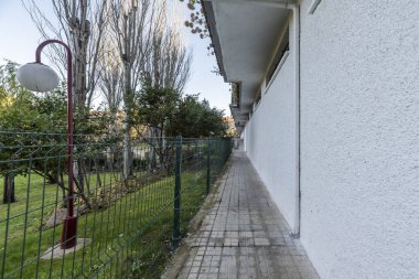 Çimenli ve manikürlü çitleri olan manzaralı ortak alanları olan yerleşim yerinin etrafındaki metal çitli dış çevre koridoru.