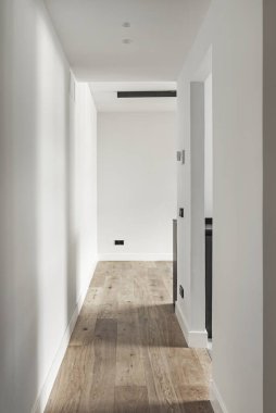 Ahşap zeminli ve düz beyaz duvarlı odalara erişimi olan bir evin koridoru.