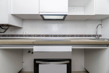 Ön görüntüde meşe rengi ahşap tezgahlı ev mutfağı, sapı olmayan beyaz mobilyalar ve bazı eşyalar için yer yok, sınırları olan beyaz fayanslar.