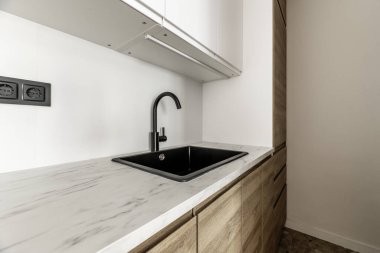 Çatı katı tipi bir evin açık mutfağı meşe ağacından mobilyalar, siyah reçine lavabosu.