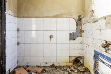 Harap olmuş bir evin içinde, bir sürü kir ve kırık beyaz kiremit duvarlı enkaz var.