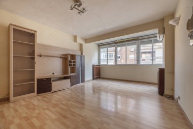 İçinde gevşek mobilyalar, ucuz ahşap döşemeler ve alüminyum pencereli büyük bir pencere olan bir oturma odası.