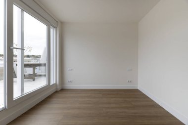 Ahşap zeminli panoramik bir oturma odası manzarası ve cam bölmeden bir apartmanın terasına erişim.