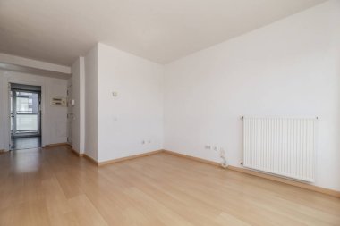 Sade beyaz duvarları, açık ahşap döşemeleri ve ucuz alüminyum kaloriferleri olan boş bir oda.