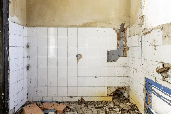 Harap olmuş bir evin içinde, bir sürü kir ve kırık beyaz kiremit duvarlı enkaz var.