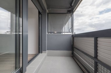 Gri kumaş tenteli, gri alüminyum, cam erişimi ve gri terrazzo zeminli bir evin terası.