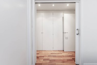 Yatak odasının çıkışında, duvarda sürgülü kapılar, kırmızı parke döşemeler ve beyaz ahşap dolaplar olan bir soyunma odası.