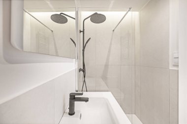 Oval porselen lavabosu olan lüks bir spa banyosu, siyah musluklar ve aromaterapi sistemi olan cam bir duş muhafazası.