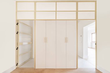 Yürüme odasının kapısı, kutsanmış alüminyum çerçeveler ve saydam camlarla, mat beyaz dolaplarla çelişiyor.