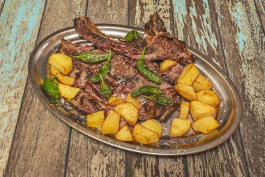 Kömürün üstünde ızgara Charolais bifteği, yanında patates, aioli ve kızarmış vişneli domatesle servis edilir.