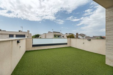 Çatı katındaki gevşeme alanı mermer duvarlarla yapay çimenliğin parlak yeşiliyle çelişiyor.