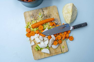 Açık mavi bir masada bambu ağacından yapılmış mutfak sahnesinde taze soyulmuş şalgam, yıkanmış havuç ve güveç için taze soğan gösteriliyor.