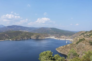 Açık bir günde, su deposunun yamaçlarında ve turkuaz sularında yoğun yeşil renkte bahar panoraması