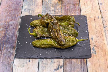 Kızarmış yeşil biberli geleneksel yemek tavadan taze çıkmış, kaba tuz serpiştirilmiş ve kil tabakta servis edilmiş..