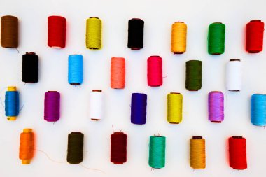Beyaz arkaplanda çok renkli iplik bobinleri.