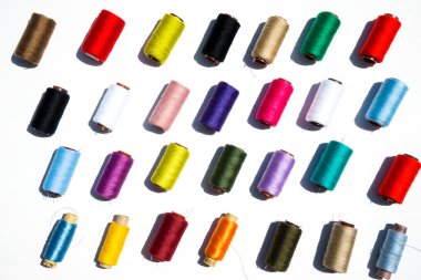 Beyaz arkaplanda çok renkli iplik bobinleri.