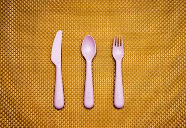 Pembe, plastik kaşık, çatal, bıçak kahverengi arka planda..