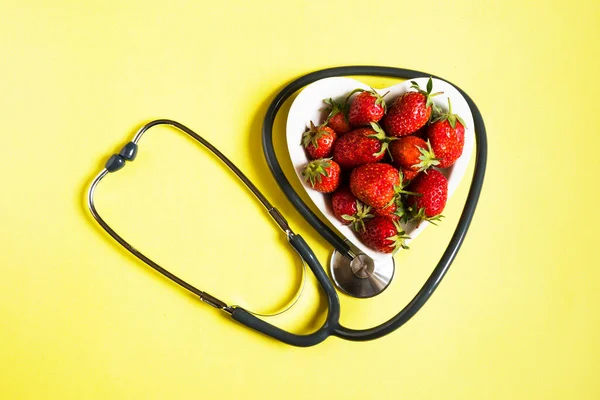 健康の概念 黄色の背景に聴診器を備えた新鮮なイチゴ トップビュー — ストック写真