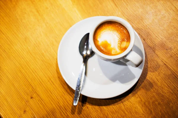 一个白色的杯子和茶托 茶托上有咖啡和棕色的木制桌子 — 图库照片
