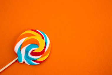 Çubukta renkli spiral lolipop şekeri. Turuncu bir arkaplanda.