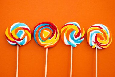 Çubukta renkli spiral lolipop şekeri. Turuncu bir arkaplanda.