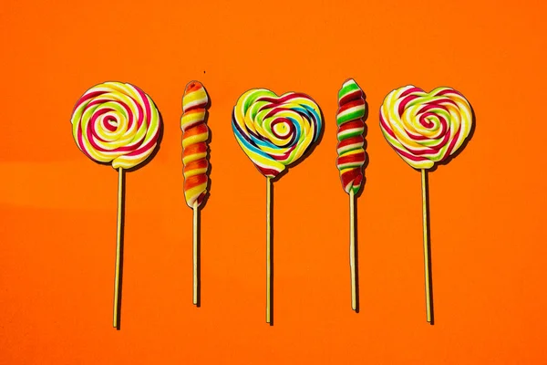Colorful spiral lollipop candy on stick. On a orange background.