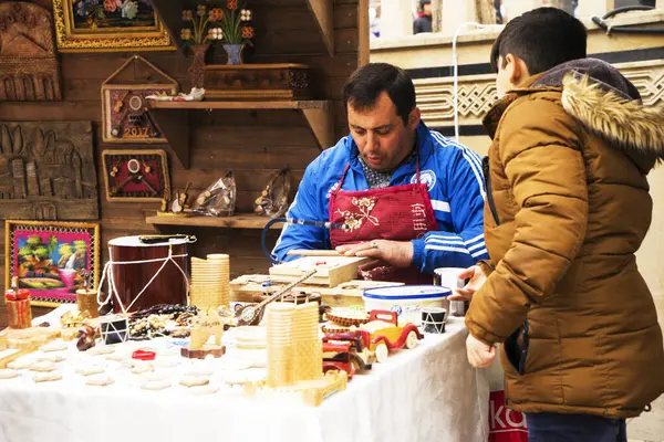 Stock image BAKU, AZERBAIJAN - JANUARY 24, 2022: A craftsman sits at a table and prepares souvenirs from wood. A workshop for wood processing or wood carving near the street market. there are many wooden souvenirs and products around it