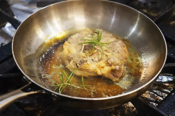 A piece of lamb leg is fried in oil in an iron pan.