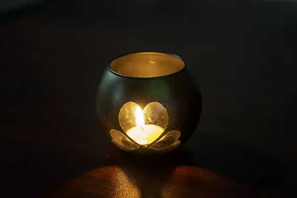 A handmade candle holder. A candle holder made of a glass jar, in the shape of a heart, stands on a table in a dark room. Valentine\'s Day, decoration, romantic atmosphere.