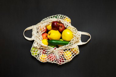 Siyah arka planda farklı sebzeler ve meyveler olan beyaz ip torbası. en üstteki görünüm