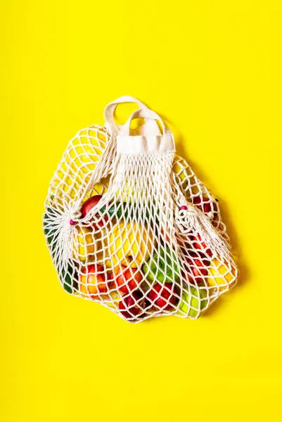 White string bag with different vegetables and fruits on a yellow background. top view