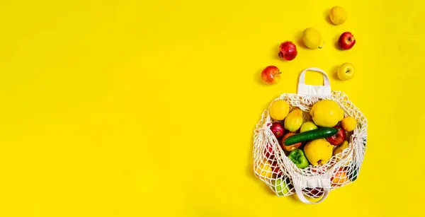 White string bag with different vegetables and fruits on a yellow background. top view