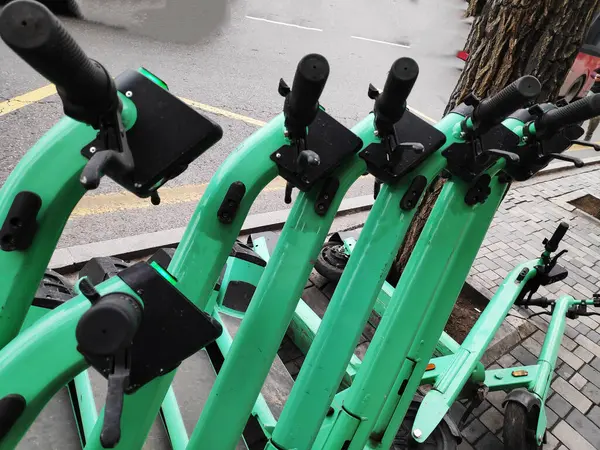 Shared Electric Scooters Parked in Row in Street. Cropped View of Green Shared E-Scooters Neatly Parked next to each other on Sidewalk in Street.