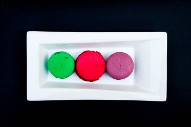 colored macaroons on a white plate on a black background. clipart