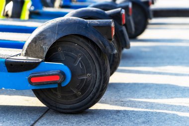 Otoparka park edilmiş kiralık mavi elektrikli scooterlar kullanıma hazır. Çevreyi kirletmeden etrafta dolaşmanızı sağlayan çok tanıdık bir araç. Çevre dostu ulaşım. Tekerlekler yakın çekim.