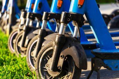 Otoparka park edilmiş kiralık mavi elektrikli scooterlar kullanıma hazır. Çevreyi kirletmeden etrafta dolaşmanızı sağlayan çok tanıdık bir araç. Çevre dostu ulaşım. Tekerlekler yakın çekim.