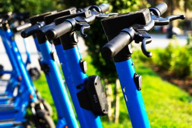 Otoparka park edilmiş kiralık mavi elektrikli scooterlar kullanıma hazır. Çevreyi kirletmeden etrafta dolaşmanızı sağlayan çok tanıdık bir araç. Çevre dostu ulaşım. Direksiyona yakın çekim