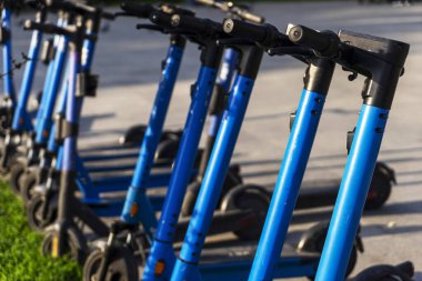 Otoparka park edilmiş kiralık mavi elektrikli scooterlar kullanıma hazır. Çevreyi kirletmeden etrafta dolaşmanızı sağlayan çok tanıdık bir araç. Çevre dostu ulaşım. Direksiyona yakın çekim