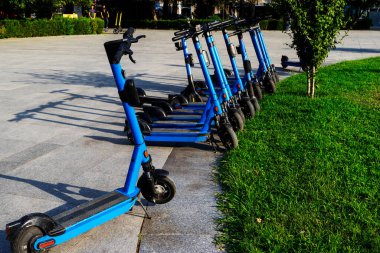 Otoparka park edilmiş kiralık mavi elektrikli scooterlar kullanıma hazır. Çevreyi kirletmeden etrafta dolaşmanızı sağlayan çok tanıdık bir araç. Çevre dostu ulaşım.