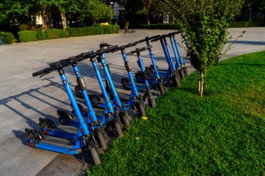 Otoparka park edilmiş kiralık mavi elektrikli scooterlar kullanıma hazır. Çevreyi kirletmeden etrafta dolaşmanızı sağlayan çok tanıdık bir araç. Çevre dostu ulaşım.