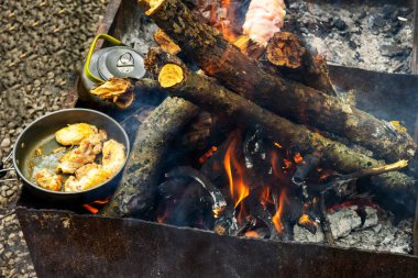 Metal bir ızgaranın üzerinde tavuklu dökme demir bir tava duruyor. Açık ateşte yemek pişirmek. Kamp gezisinde ve piknikte nefis yemekler..