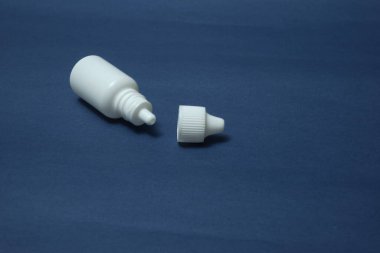 Beyaz bir şişe, göz şişesi ve mavi bir arka planda burun damlası.